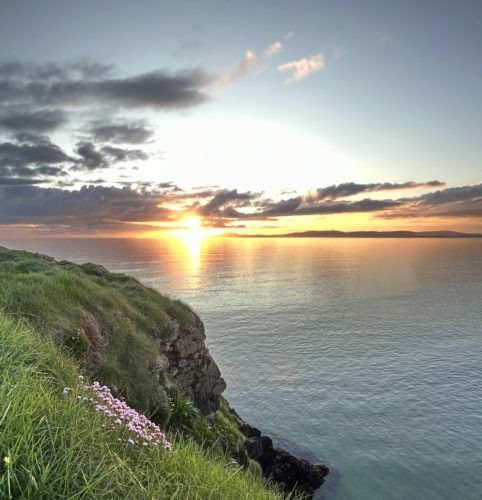 Green cliff in Bundoran with ocean and sunset.